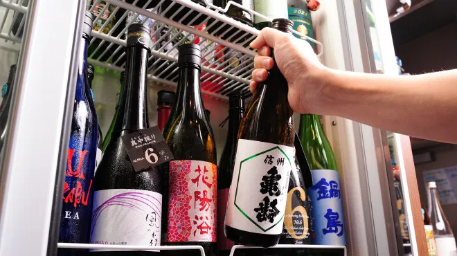 A hand selecting a sake bottle from a refrigerator